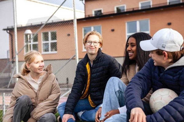 Group of diverse teens hanging out and laughing outside of school.