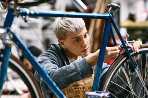 A young adult employee in a bike shop tightens the brakes on the back wheel of a road bicycle.
