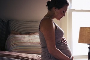 A pregnant young woman is sitting on the bed at home, tenderly holding her belly.