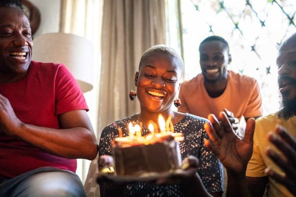 A young woman is holding a birthday cake and celebrating with family and friends.