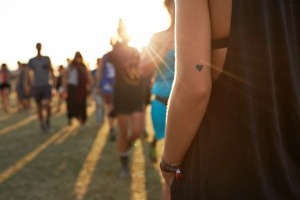 Rearview of woman's arm with heart-shaped tattoo standing at an outdoor music festival.