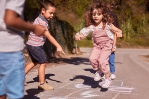 Group of young kids playing hopscotch on sidewalk.