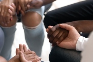 Diverse people sitting in circle holding hands at group therapy