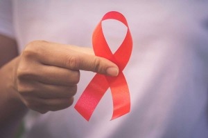 Close-up of a woman's hand holding a red awareness ribbon.