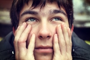 close up of a young man who rests his hands on his face.