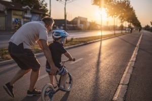 Adult man helping a young boy to ride a bike on a neighborhood street.