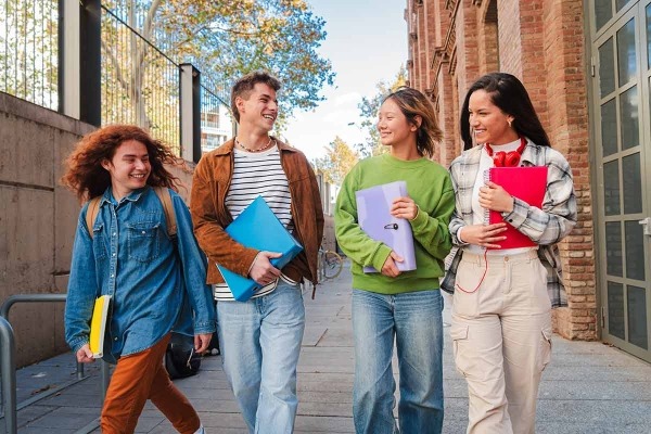 Four happy teenagers walking with notebooks.