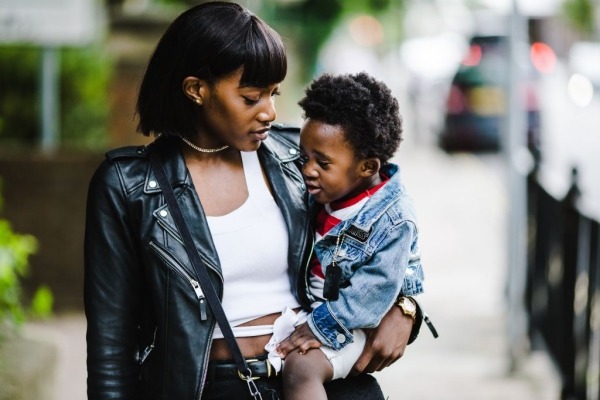 research in genetic studies Black woman holding a toddler and walking down a city street.