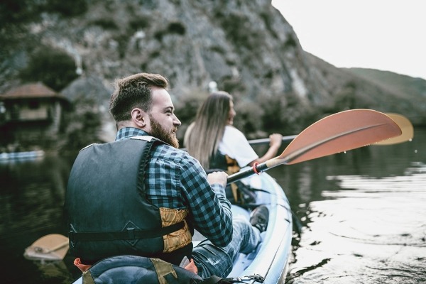 Un hombre y una mujer usan chalecos salvavidas y reman en un río rodeado de montañas.