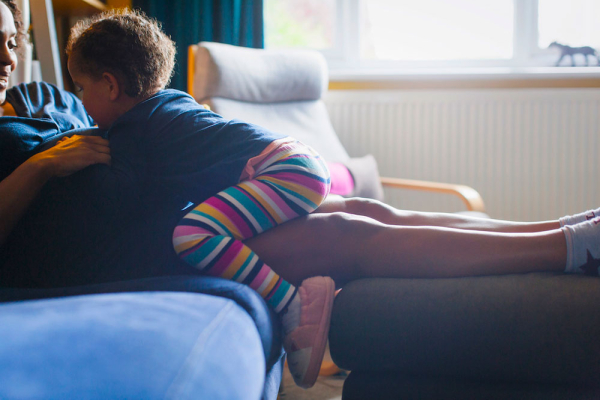 A young girl sitting on the couch and touching her pregnant mother's stomach.