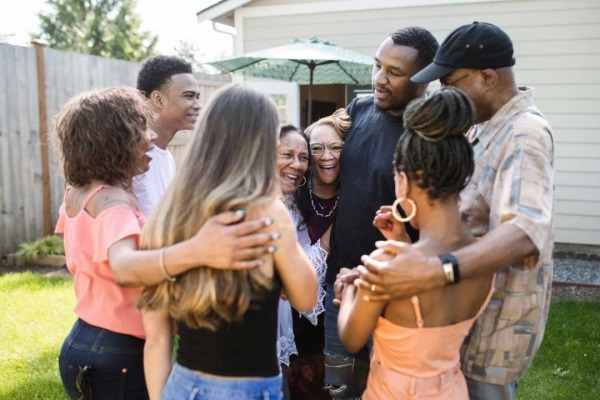 Multi-generational and diverse group of eight adults smiling and embracing.