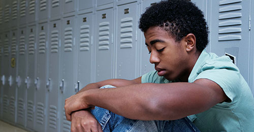 Teen boy sitting against lockers thinking. 