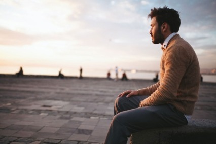 Young man sitting on a pier looking away from the camera and watching the sunset.